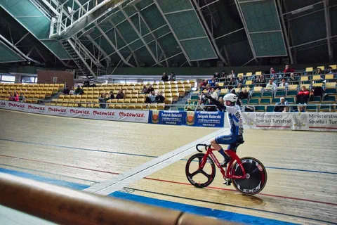 Młody zawodnik na czerwonym rowerze torowym przygotowujący się do startu przy linii z sędzią