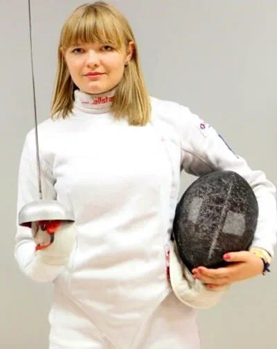 Szpadzistka Aleksandra Zamachowska w białym stroju szermierczym ze szpadą i maską.