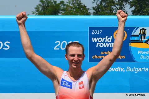 Zawodnik na podium unoszący obie ręce w geście triumfu na tle baneru mistrzostw w Płowdiw